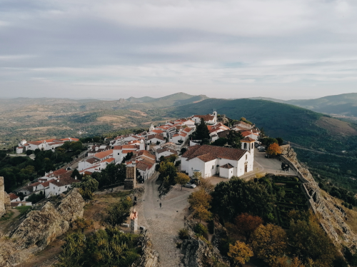alt="Aerial view of a traditional whitewashed hilltop village with red-tiled roofs in Portugal