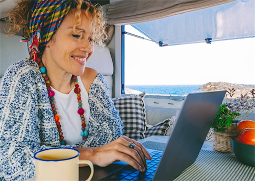 Woman working on a laptop inside a camper van with a sea view
