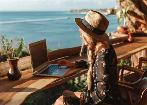 Woman using a laptop at an outdoor desk with an ocean view