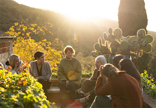 Group of digital nomads sitting and talking in a Tuscan garden at sunset