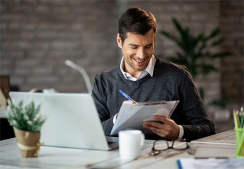 Man working at desk with laptop and clipboard in office