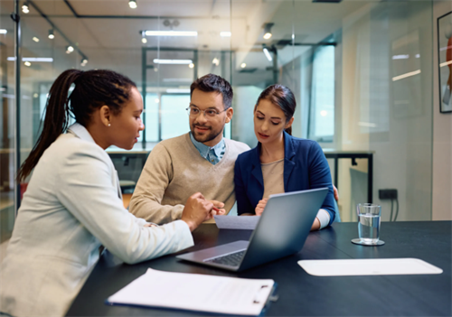 Three business professionals discussing documents around a laptop in a modern office