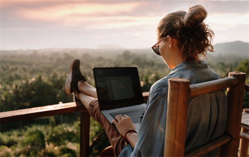 Woman working on a laptop outdoors with a scenic sunset view